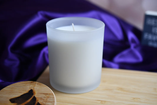 Single wicked, frosted white candle with purple satin in the background.