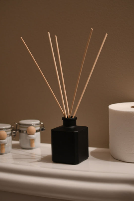 Matte Black square diffuser bottle with 5 reeds sticking out of it in a natural home bathroom setting.
