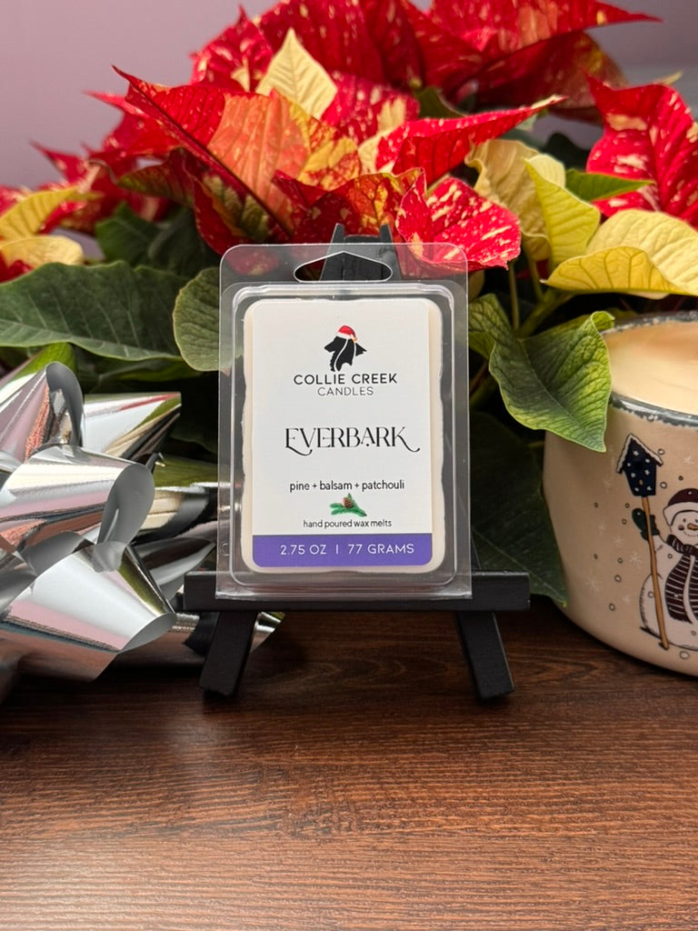 Collie Creek Candles Everbark wax melt packaging with poinsettias and a silver bow in the background.