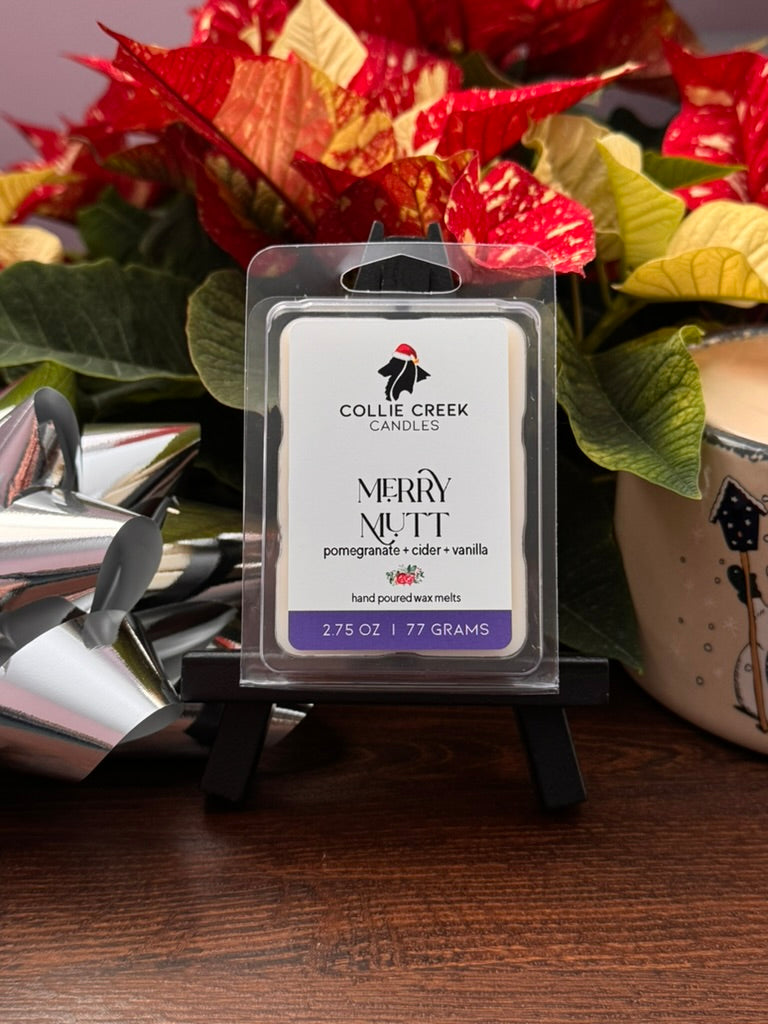 Collie Creek Candles wax melt Merry Mutt with holiday-themed packaging in front of poinsettias.