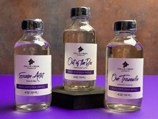 Collection of 3 diffuser refill bottles labeled with purple and back lettering. The bottles have black tops and are shrink wrapped for shipping.
