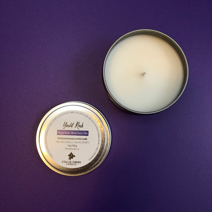 A 5oz tin candle with a label reading 'Yacht Rock' and a description of the fragrance. The candle is on a purple background.