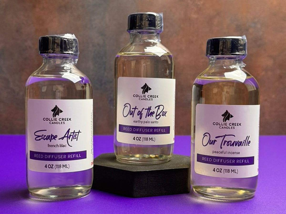 Collection of 3 diffuser refill bottles labeled with purple and back lettering. The bottles have black tops and are shrink wrapped for shipping.