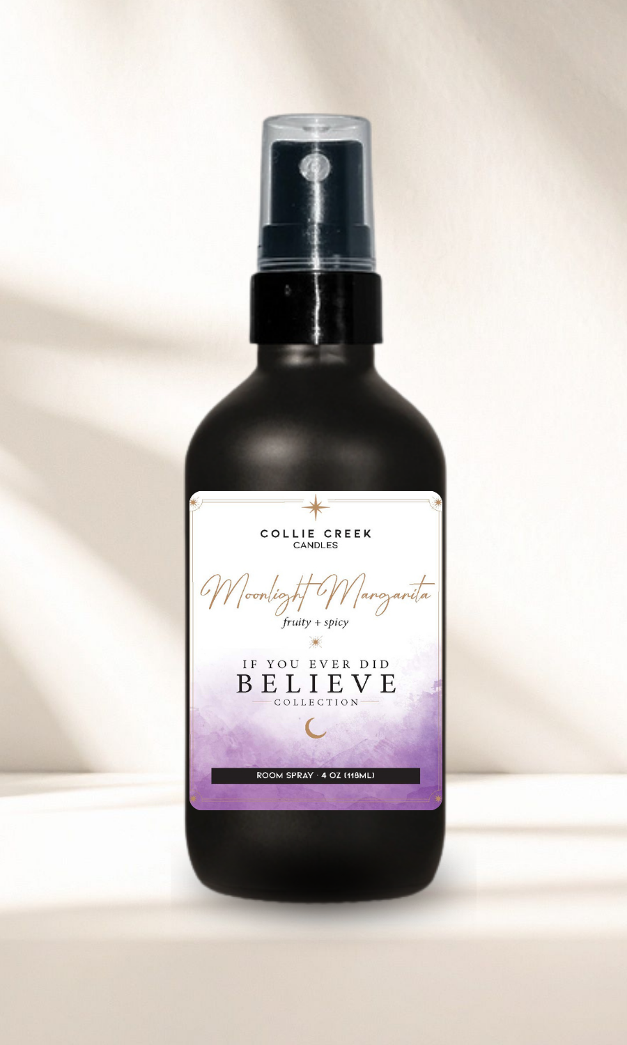 A black spray bottle of Collie Creek Candle 'Moonlight Margarita' room spray, featuring a white and purple label, set against a warm beige background with soft shadows.