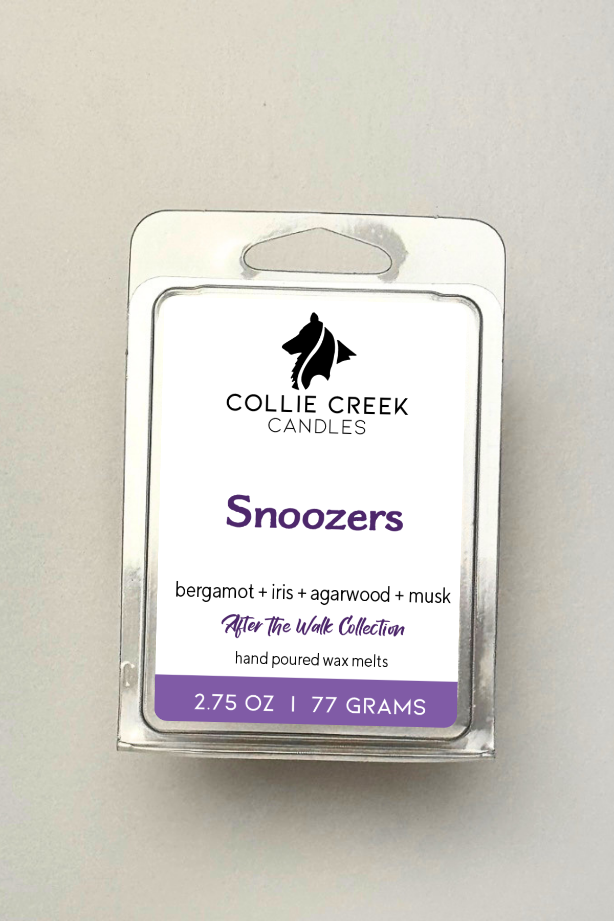 Single wax melt in a clear clam shell on a white background, Snoozers in purple on the label.