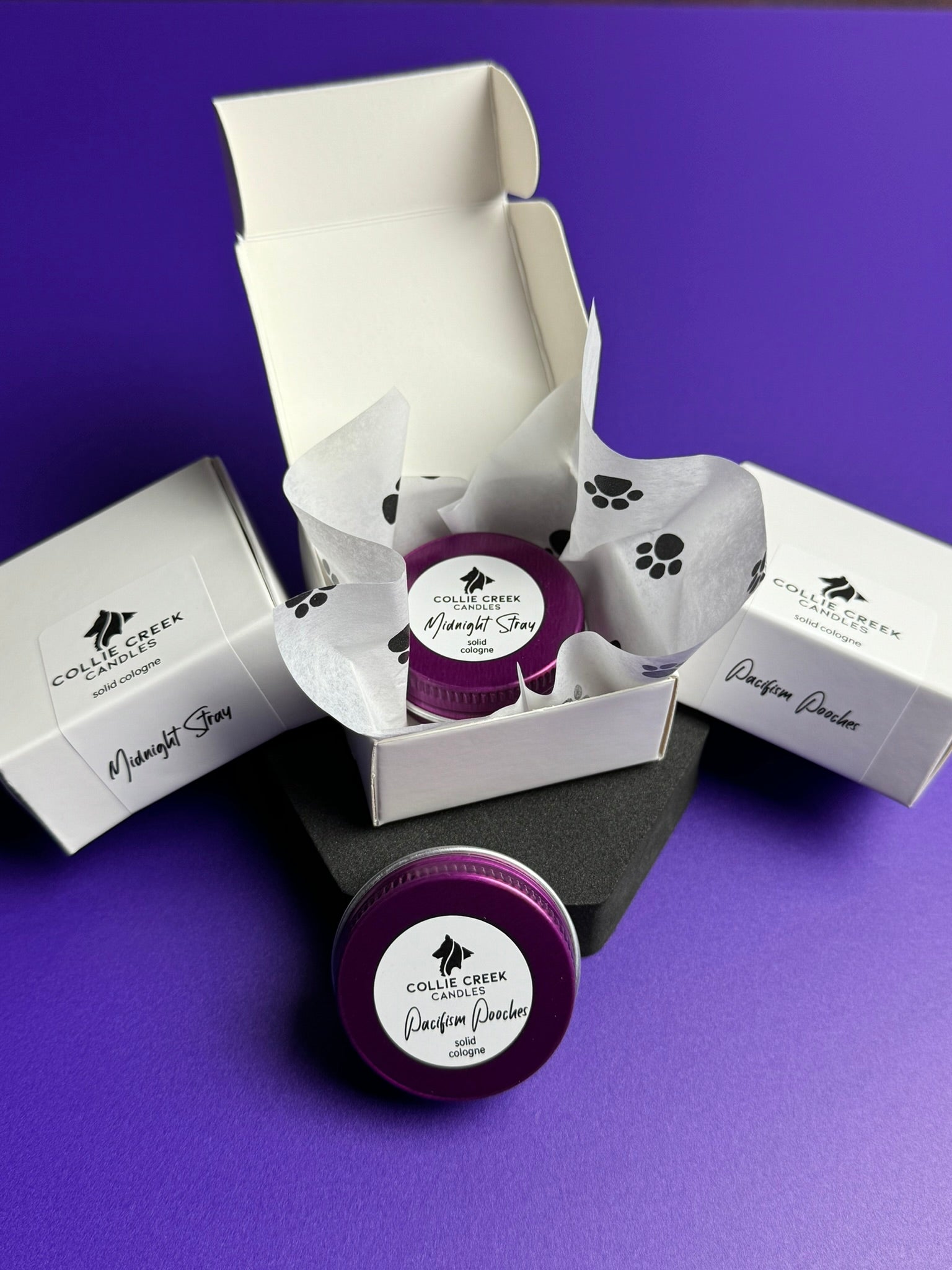 Solid colognes in lavender or patchouli scent in a purple tin and paw print tissue paper white gift box.