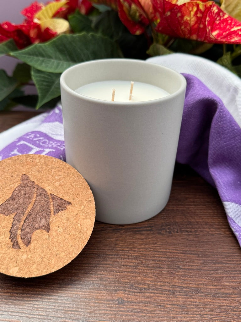 Double cotton wicked candle in stone vessel with branded cork lid in foreground.